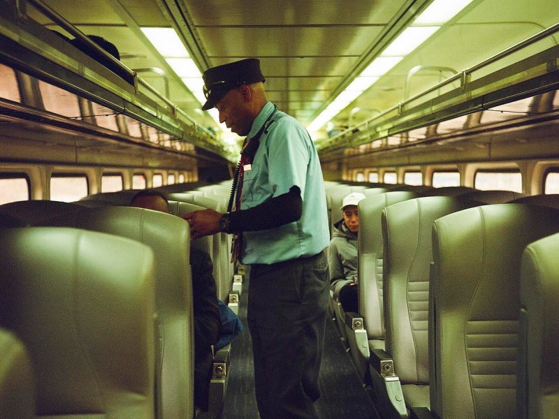 Conductor stands inside train between rows of seats.