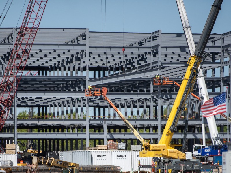 A building under construction next to two big construction cranes and an American flag