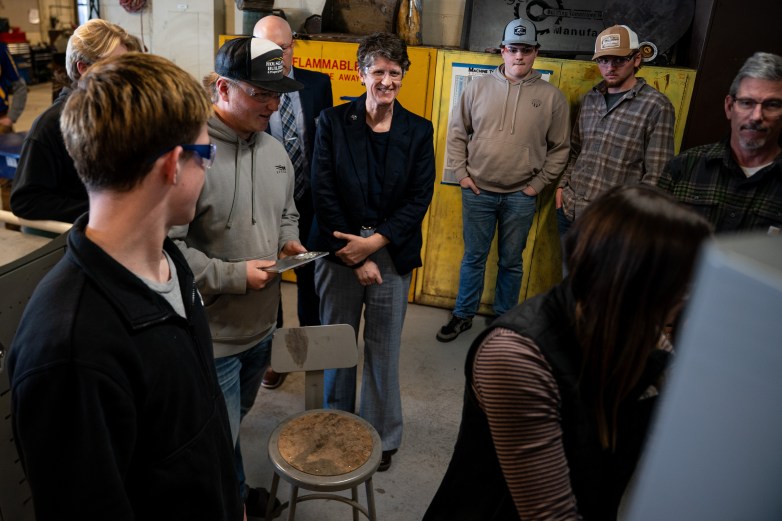 A group of people wearing safety glasses stand in a room with a chair in the middle near yellow cabinets labeled "FLAMMABLE"