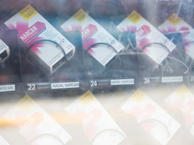 A vending machine stocked with free Narcan (naloxone) nasal spray doses, located outdoors. The machine is operated by Madison Street Medicine, and boxes labeled “NASAL NARCAN” are visible behind the glass.