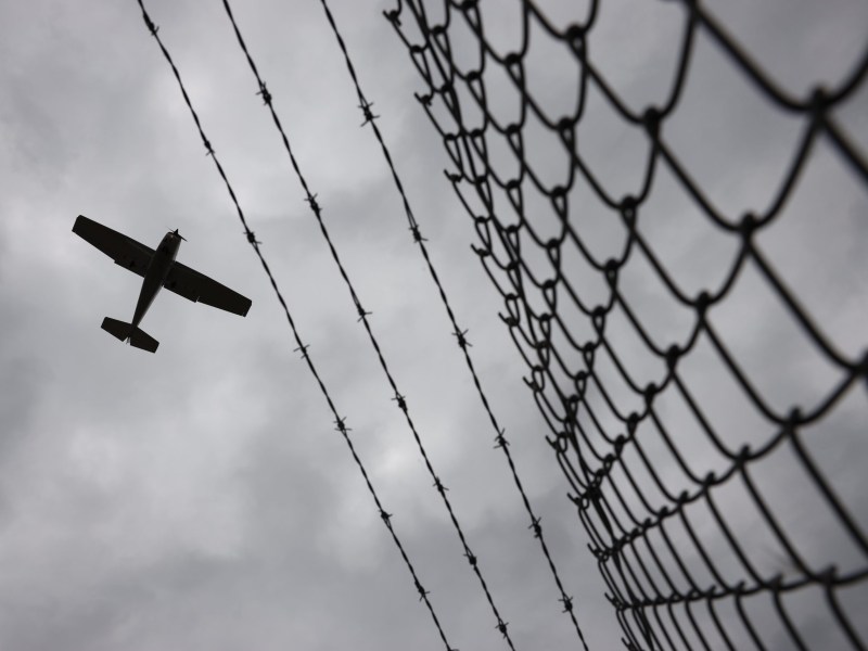 A small plane flies over a barbed wire fence