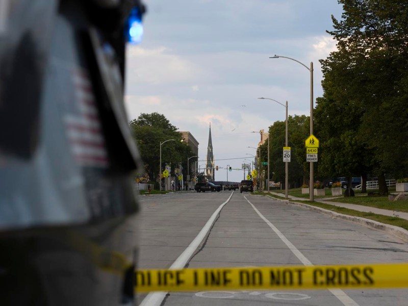 Yellow "POLICE LINE DO NOT CROSS" tape blocks a street.