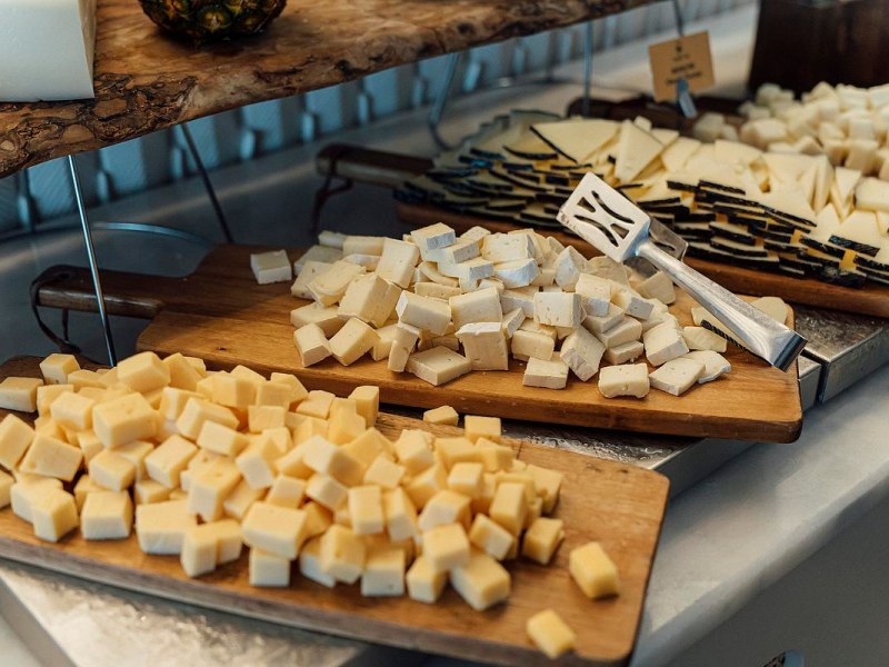 Assorted cubes and slices of cheese are arranged on wooden boards with a serving utensil placed on one of the boards.