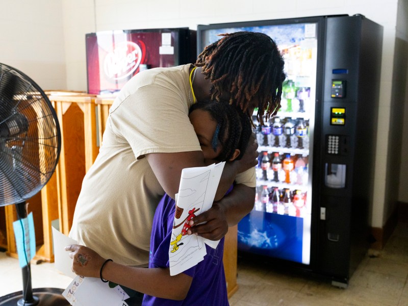 Woman hugs child in front of vending machines and a fan.