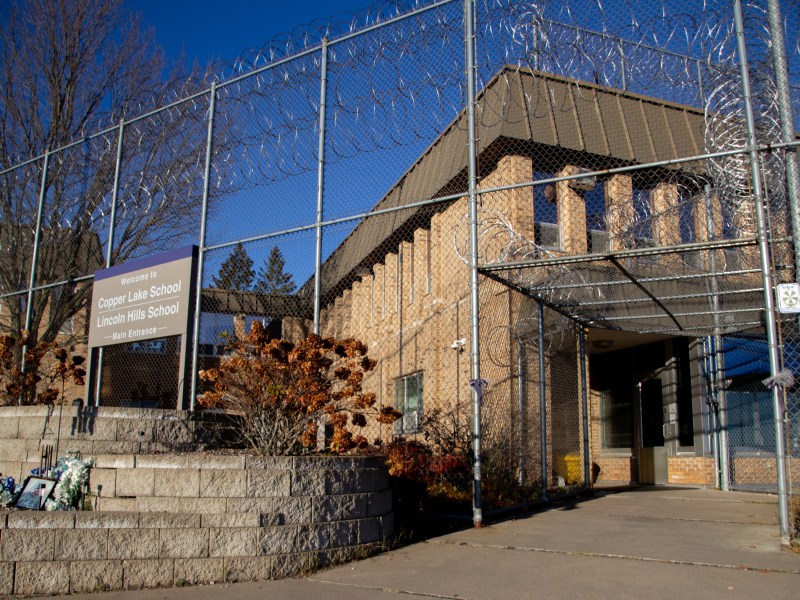 Exterior view of building and metal fence with barbed wire. Sign says “Welcome to Copper Lake School Lincoln Hills School”