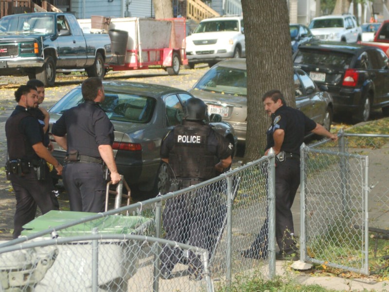 Police officers on a sidewalk between a street and a metal fence