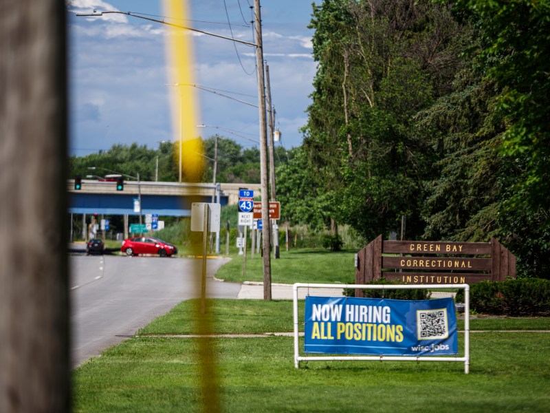 Sign says “NOW HIRING ALL POSITIONS” in front of sign that says “GREEN BAY CORRECTIONAL INSTITUTION” next to highway.