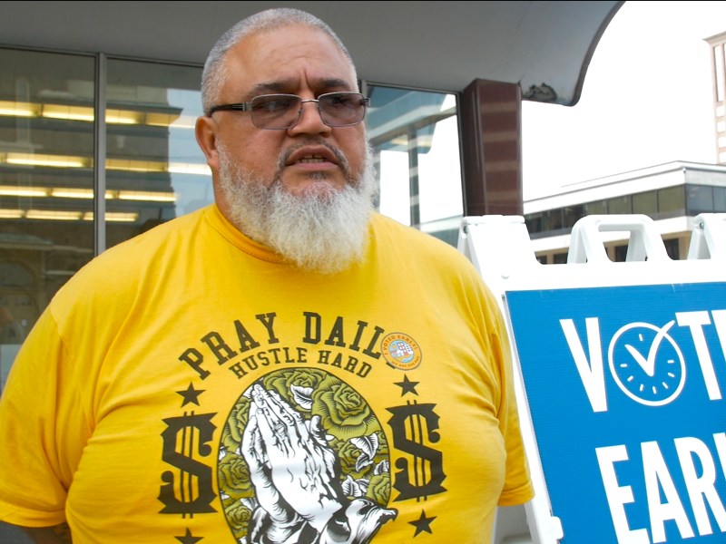 Man in yellow shirt next to a "VOTE EARLY" sign