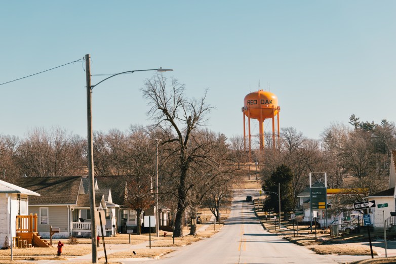 A street lined with small houses leads toward an orange water tower labeled "RED OAK," with a gas station and street signs along the road.