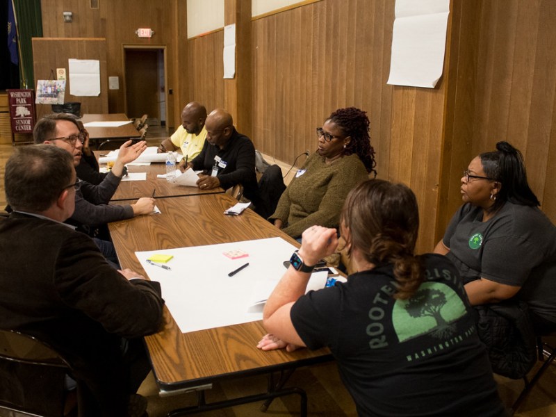 People seated around table in room with wood paneling