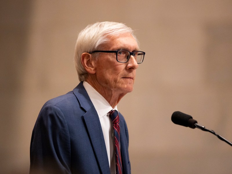 A person wearing glasses and a blue suit with a red and blue striped tie is next to a microphone.