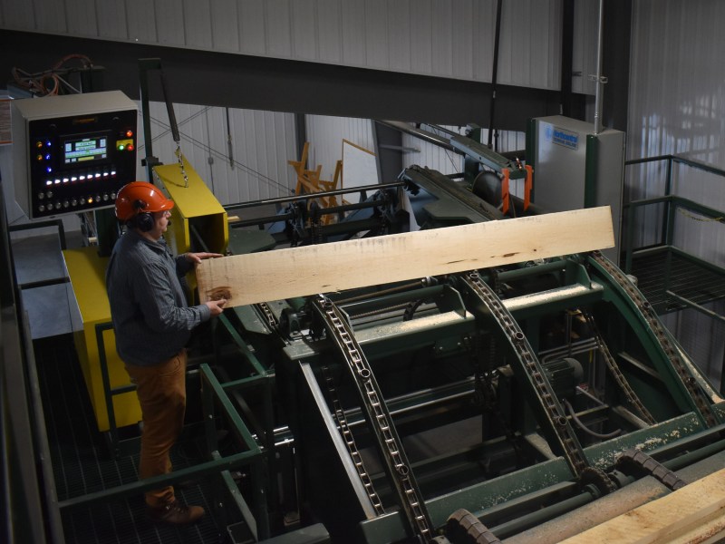 Man in hard hat holds a board above a machine.